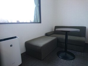 A small, private room with a single sofa, a round table, and a white air conditioning unit. - Terminal Hotel Matsuyama (Matsuyama)