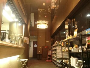 A narrow corridor with a reception desk on the left, a chandelier hanging from the ceiling, and shelves stocked with various items on the right. - Terminal Hotel Matsuyama (Matsuyama)