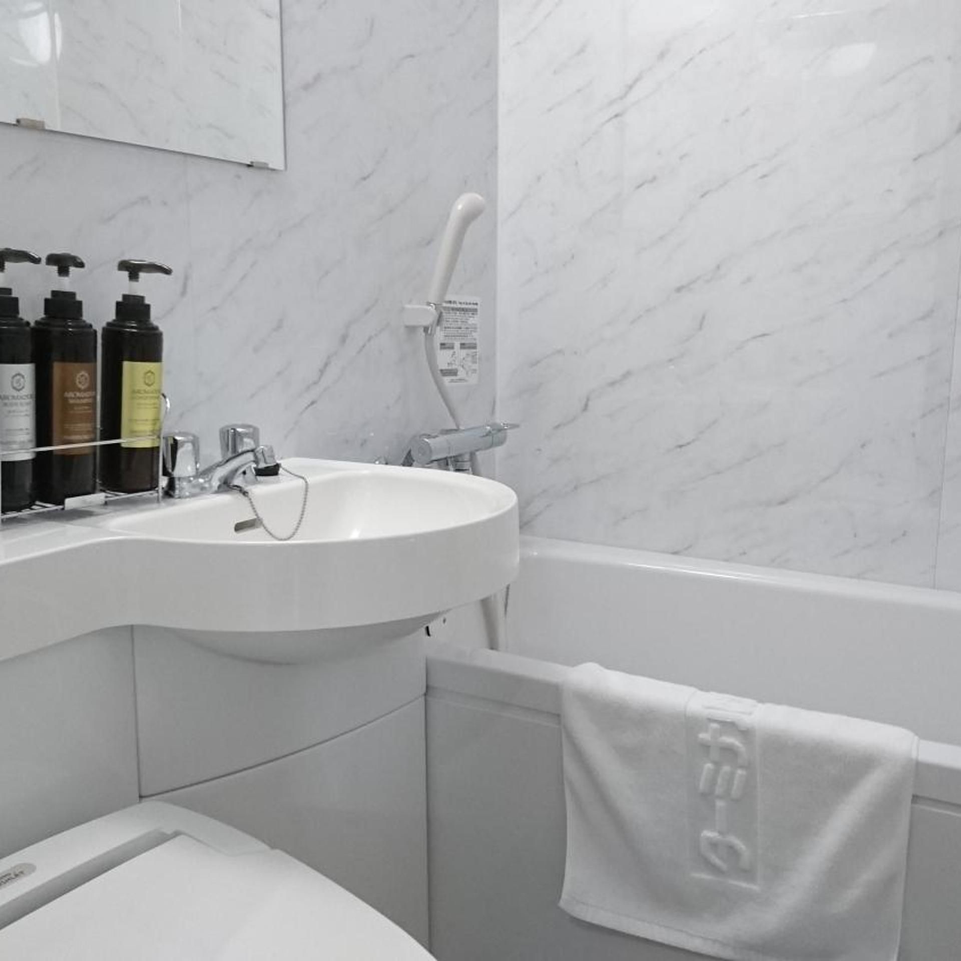 A bathroom with a white sink, a mirror above it, and a bathtub. There are toiletries on the sink's edge.