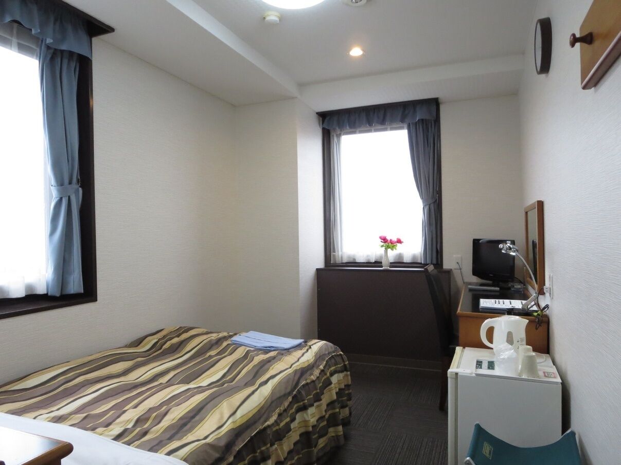 Ein Hotelzimmer mit Bett, Schreibtisch, Computer, Kaffeemaschine und einem fenster mit Vorhängen.