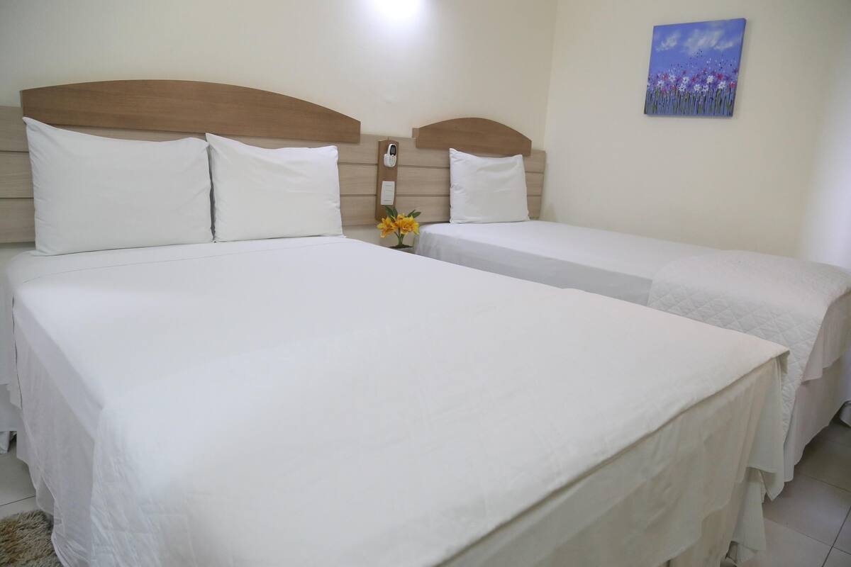 Habitación de hotel con dos camas, cabecera de madera, mesita de noche con lámpara y un cuadro en la pared.
