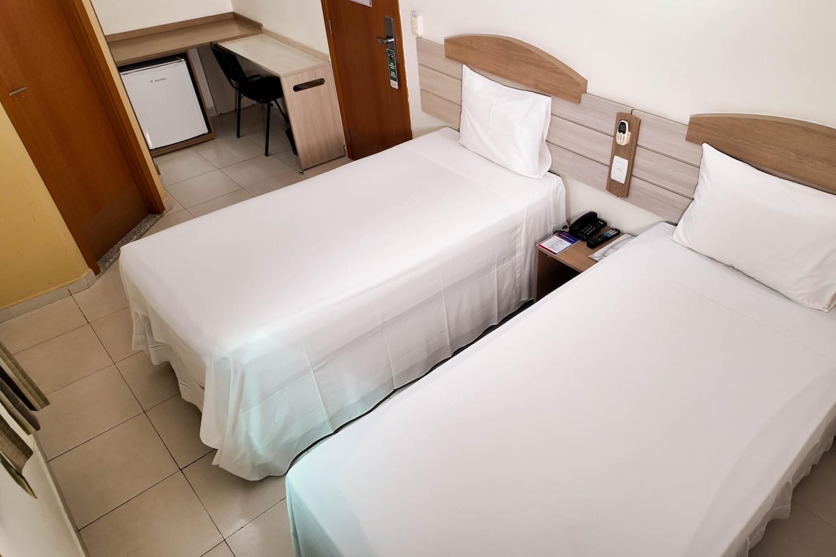 Dos camas individuales con cabeceros de madera, un escritorio y una silla en una habitación de hotel.