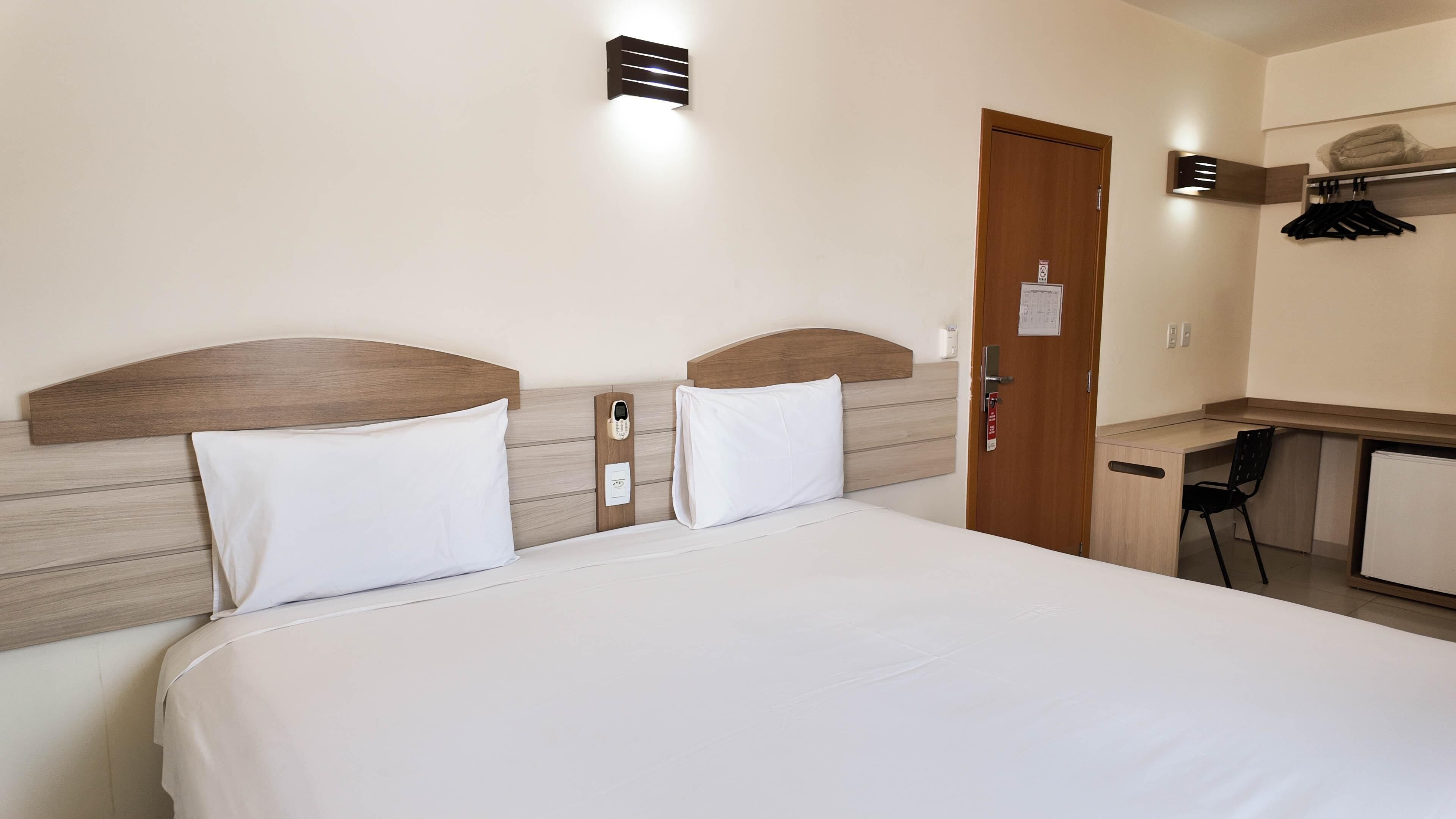A hotel room with a bed, a desk, and a door.