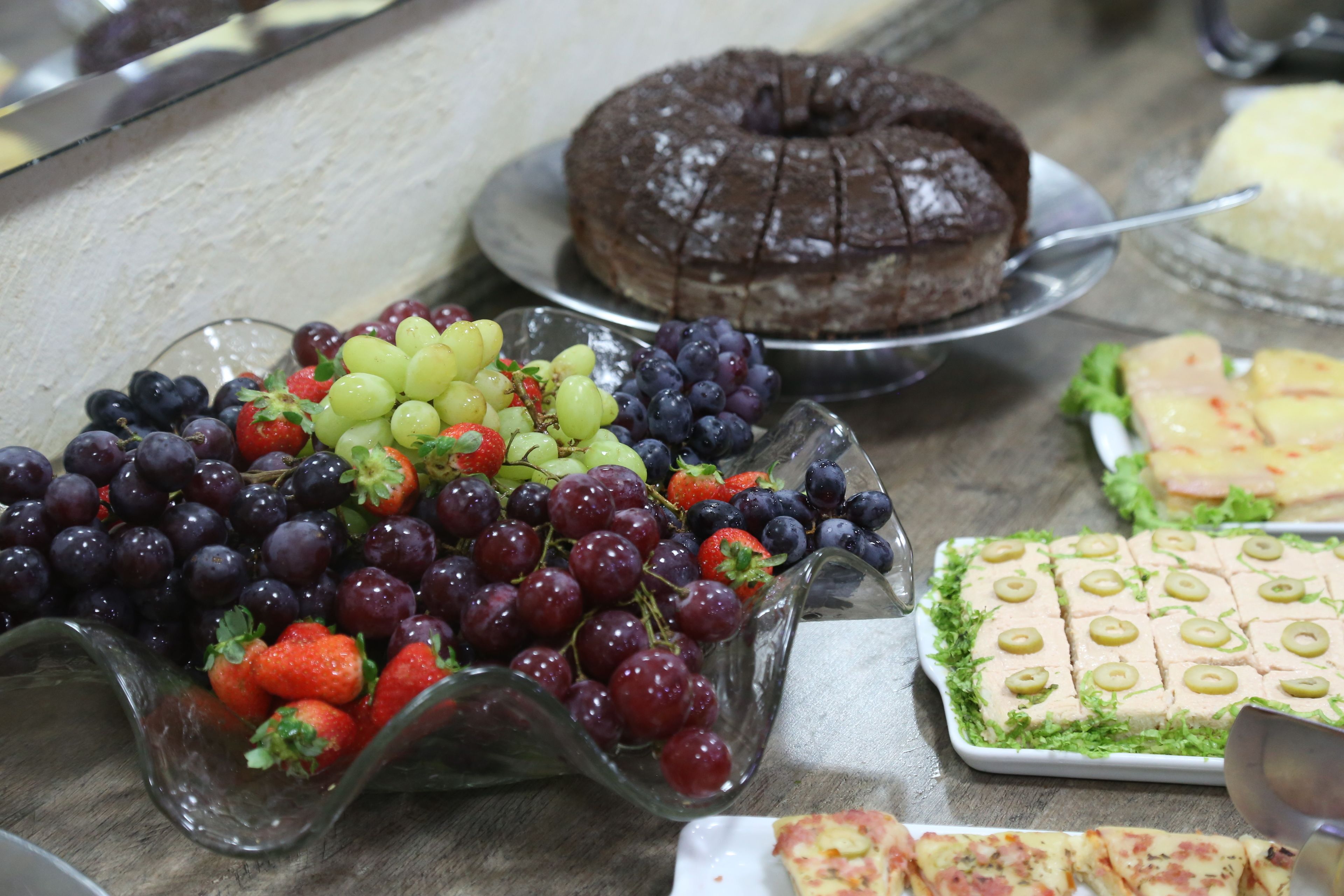 Een buffettafel met diverse gerechten, waaronder chocoladetaart, druiven, aardbeien en een schaal met olijven en kaas.