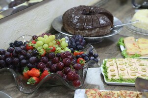 Una mesa de buffet con diversos alimentos, incluyendo un pastel de chocolate, uvas, fresas y un plato con aceitunas y queso.