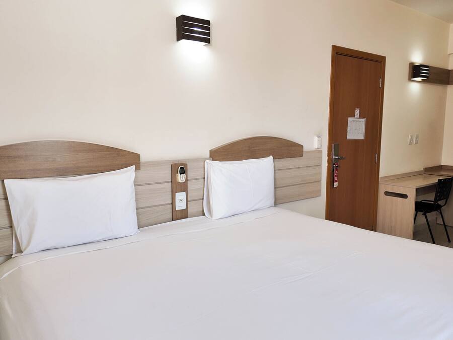 A hotel room with a bed, a desk, and a door.