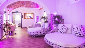 Una habitación con un arco de ladrillo, dos camas con ropa de cama estampada, una planta en maceta y un televisor montado en la pared.