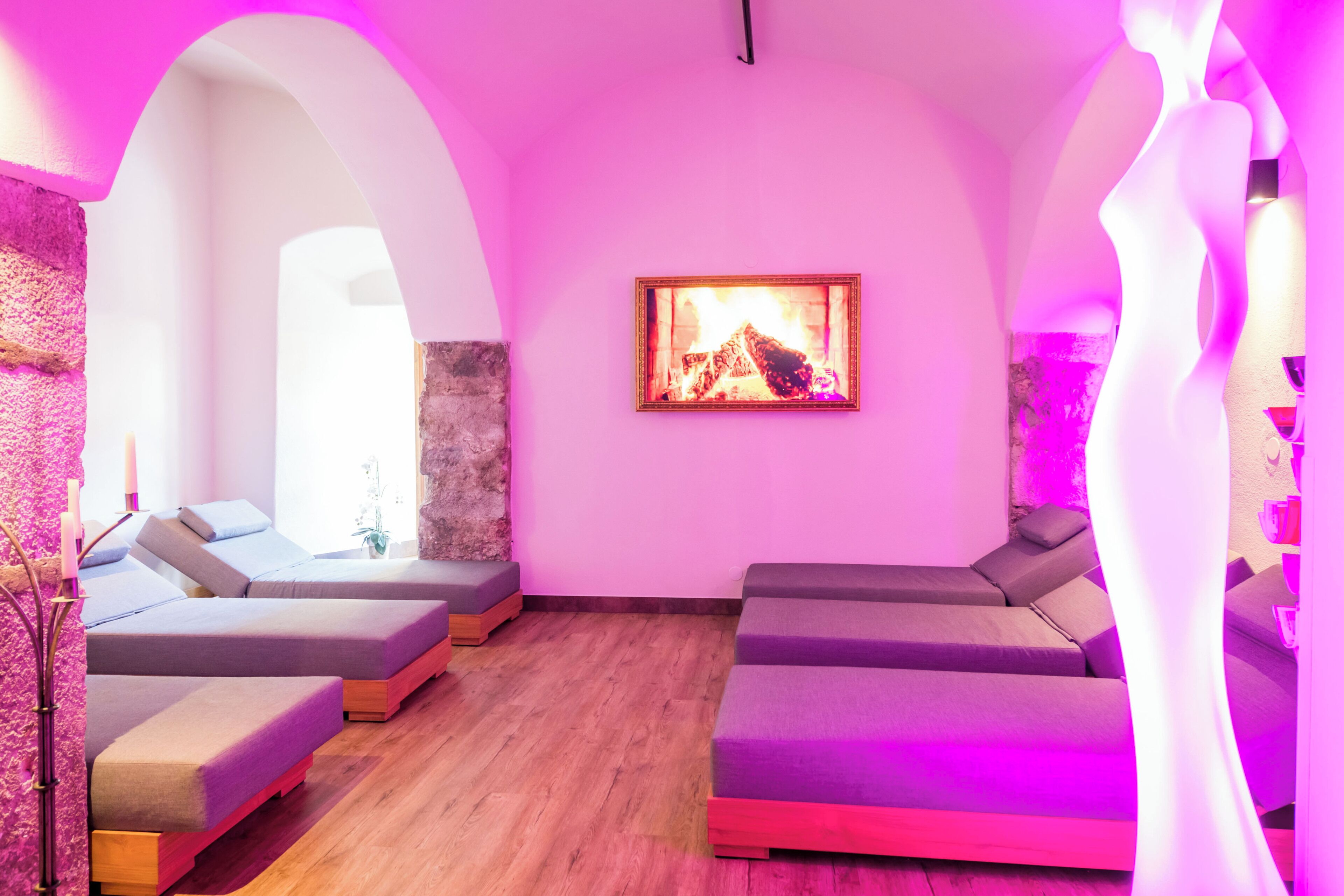 Une salle de spa dotée d’un plancher en bois, de sièges confortables, d’une cheminée et d’un éclairage d’ambiance de couleur rose.
