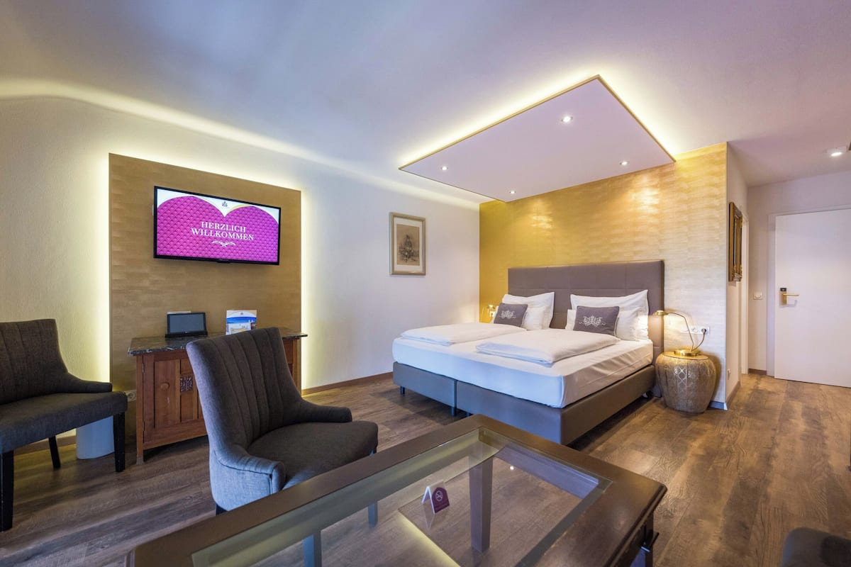 A modern hotel room with a bed, a TV, a desk, and a seating area.