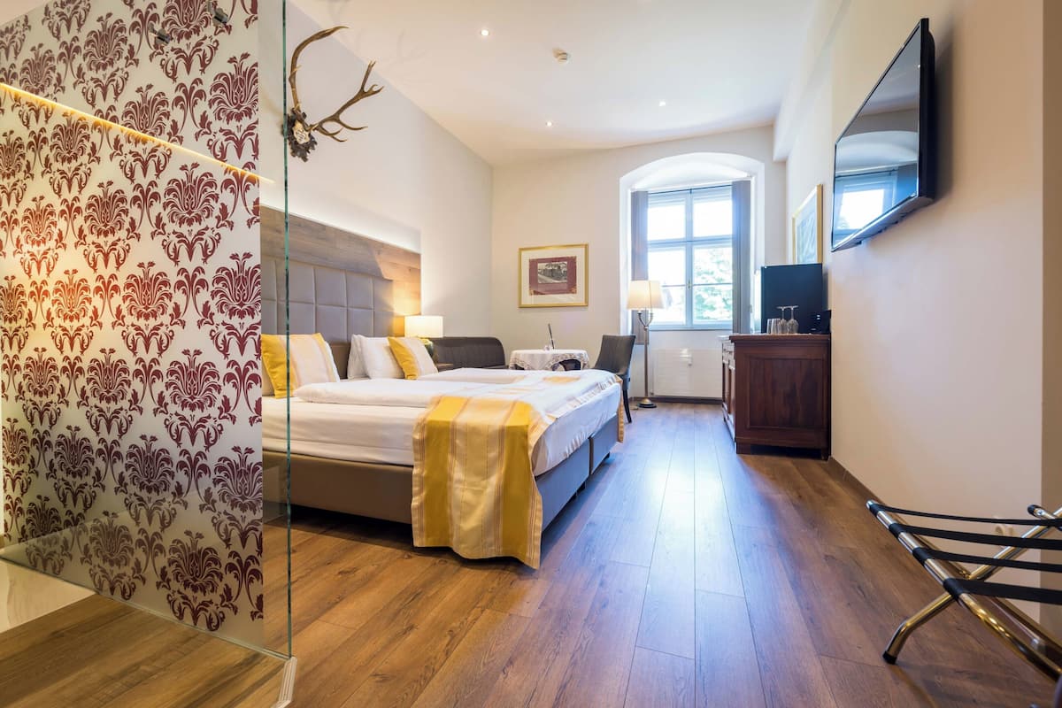 A bedroom with a bed, bedside table, lamp, TV, and a window.