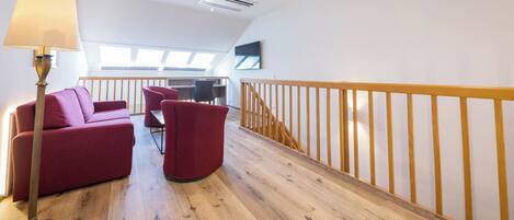 A modern interior with a wooden floor, red seating, a lamp, and a TV on the wall.