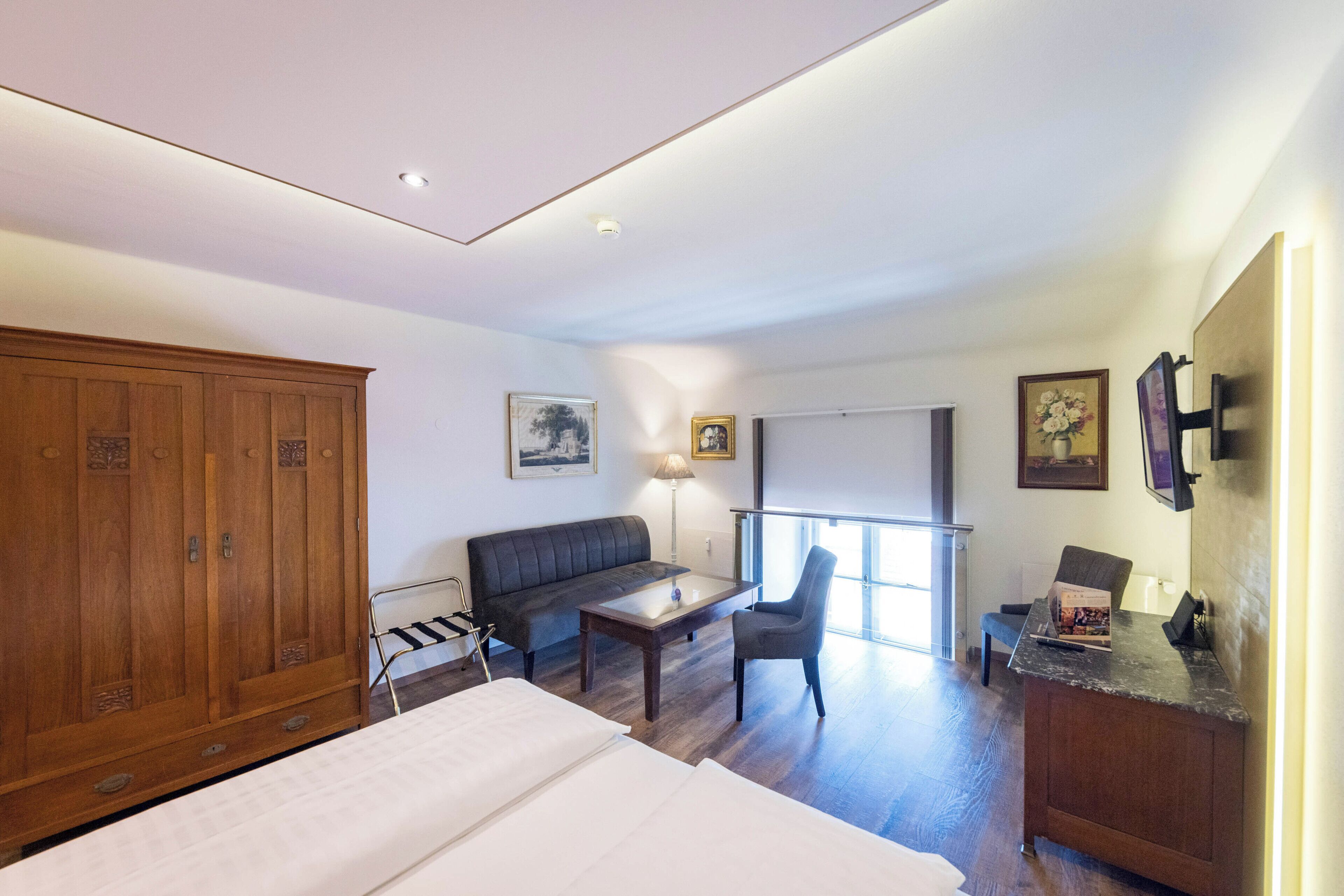 Habitación de hotel con cama, armario de madera, sofá, una mesita, una silla y escritorio con computadora.