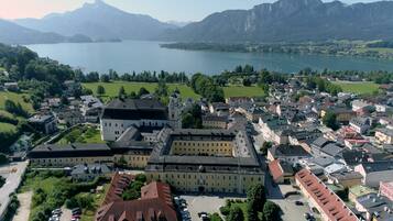 A historic building with multiple wings and a central courtyard, surrounded by a town with a lake and mountains in the background.