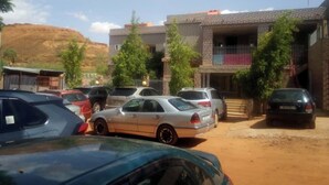 Un parcheggio con diverse auto, un edificio con un balcone e un paesaggio collinare sullo sfondo.