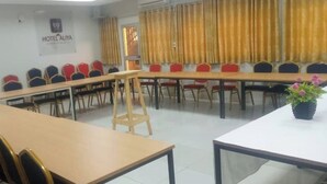 Una sala conferenze con diversi tavoli e sedie, un cartello con la scritta Hotel Aliya e una finestra con tende.