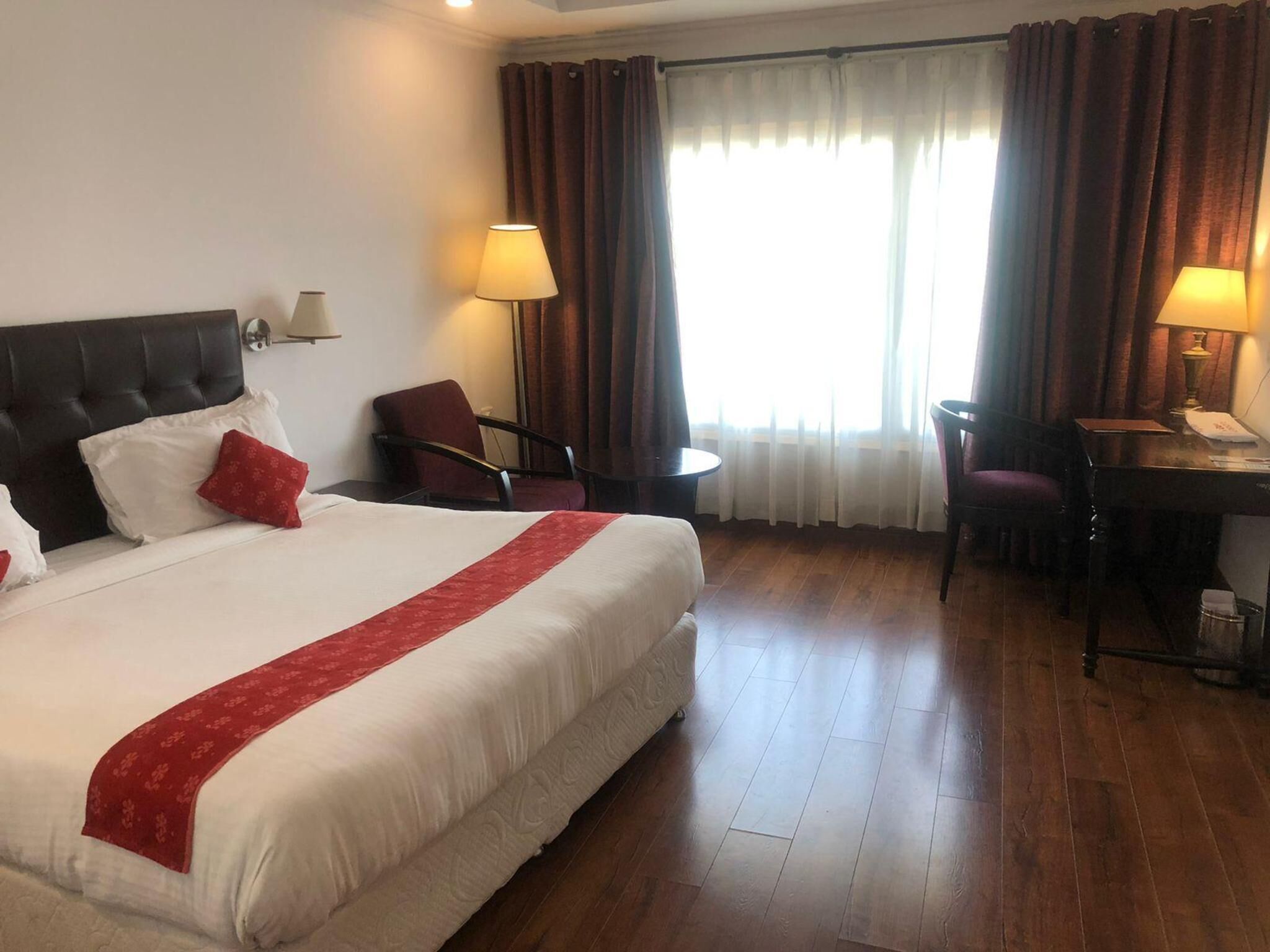 A hotel room with a large bed, two chairs, a desk, and a window with curtains.