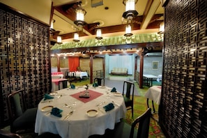 A dining area with round tables set for four, each with white tablecloths, silverware, and green napkins. - Centaur Hotel IGI Airport (New Delhi)
