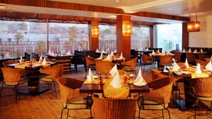 Ein Restaurant mit mehreren Tischen, Stühlen, großen Fenstern und warmer Beleuchtung.