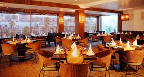Un restaurante con varias mesas y sillas, ventanas amplias e iluminación cálida.