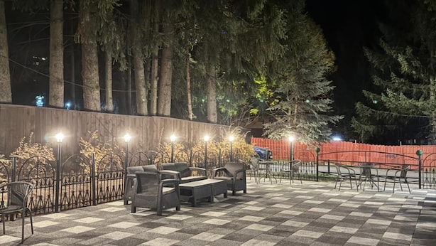 An outdoor seating area with checkered flooring and metal chairs, surrounded by trees and a wooden fence. - Rina Vista (POIANA BRASOV)