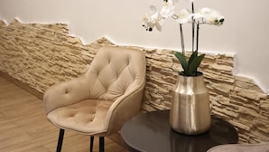 A beige upholstered armchair next to a round table with a metallic vase containing white orchids. - Rina Vista (POIANA BRASOV)