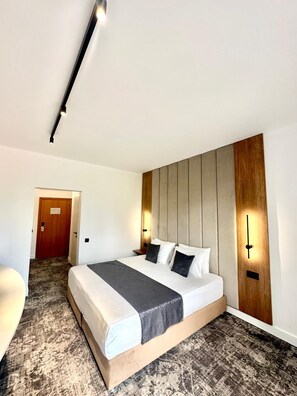 A hotel room with a large bed, a wooden headboard, two wall-mounted light fixtures, and a carpeted floor.
