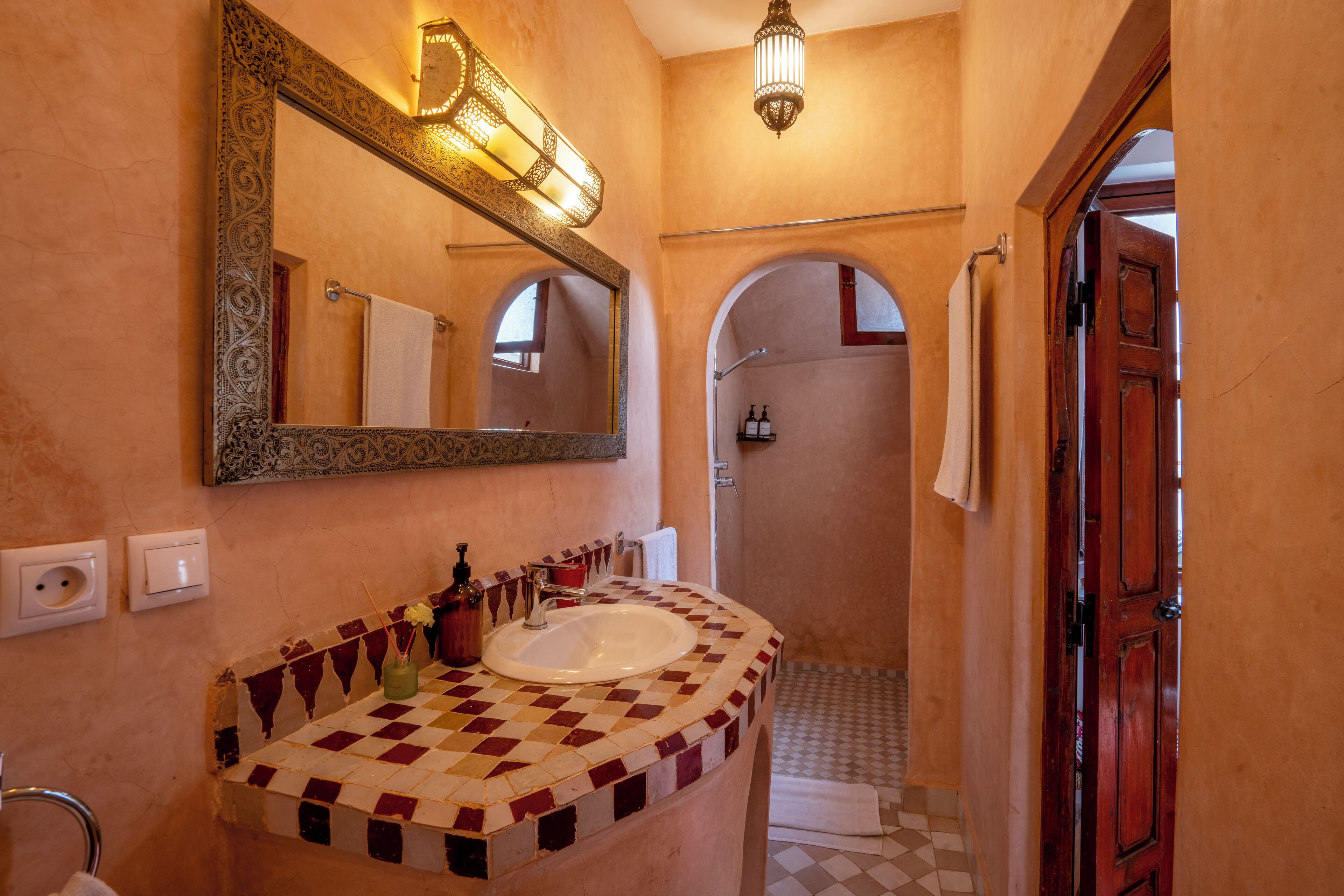 A bathroom with a checkered tile sink, a large mirror with ornate frame, and a shower area visible through an archway.