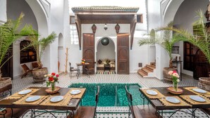 Une cour avec une piscine, un espace repas et des arcades.