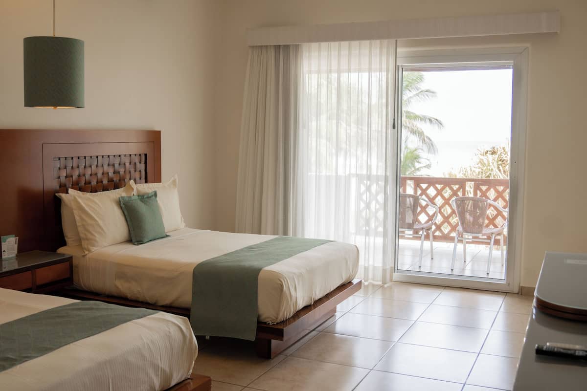 A hotel room with two beds, a balcony with a view, and a large window with curtains.