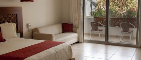 A hotel room with a large bed, a sofa, and a balcony with chairs.