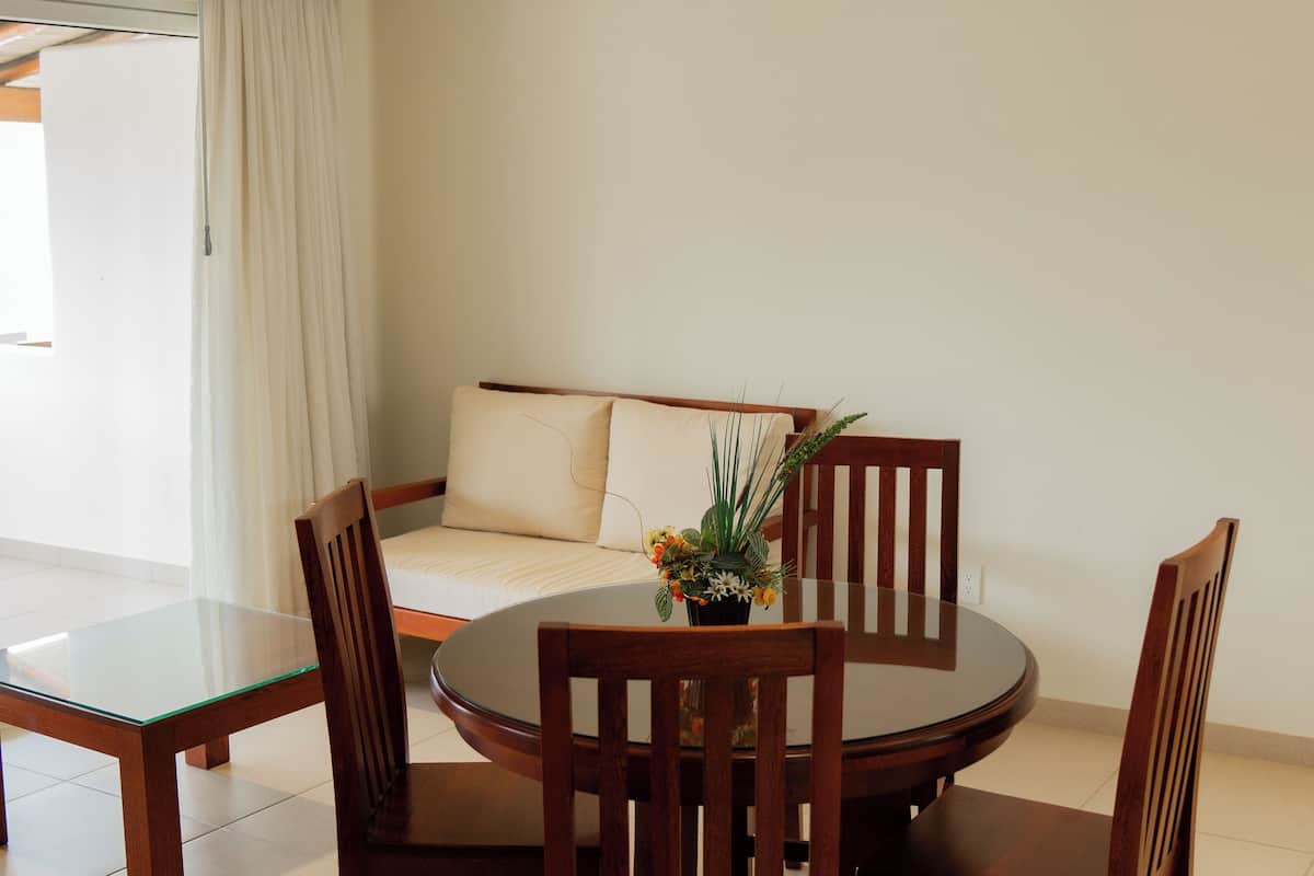 A room with a round glass table, wooden chairs, a sofa with a cushion, and a potted plant on the table.