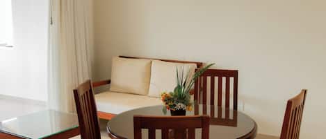Une pièce avec une table ronde en verre, des chaises en bois, un canapé avec un coussin et une plante en pot posée sur la table.