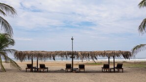 A beach with thatched umbrellas and wooden chairs facing the ocean. - Blater Hotel (Santa Maria Colotepec)