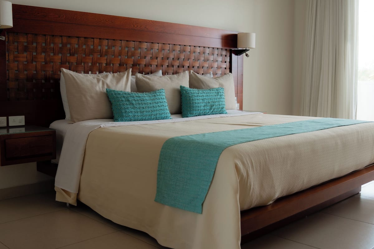 A neatly made bed with a wooden headboard, two pillows, and a teal throw blanket.