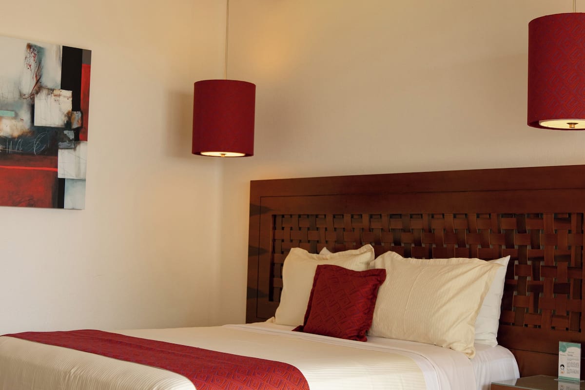 A neatly made bed with a red throw blanket, a wooden headboard, and two bedside tables with lamps.