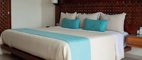 A neatly made bed with a wooden headboard, a teal throw blanket, and two teal pillows.