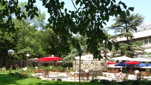 An outdoor seating area with tables and chairs, surrounded by greenery and trees.