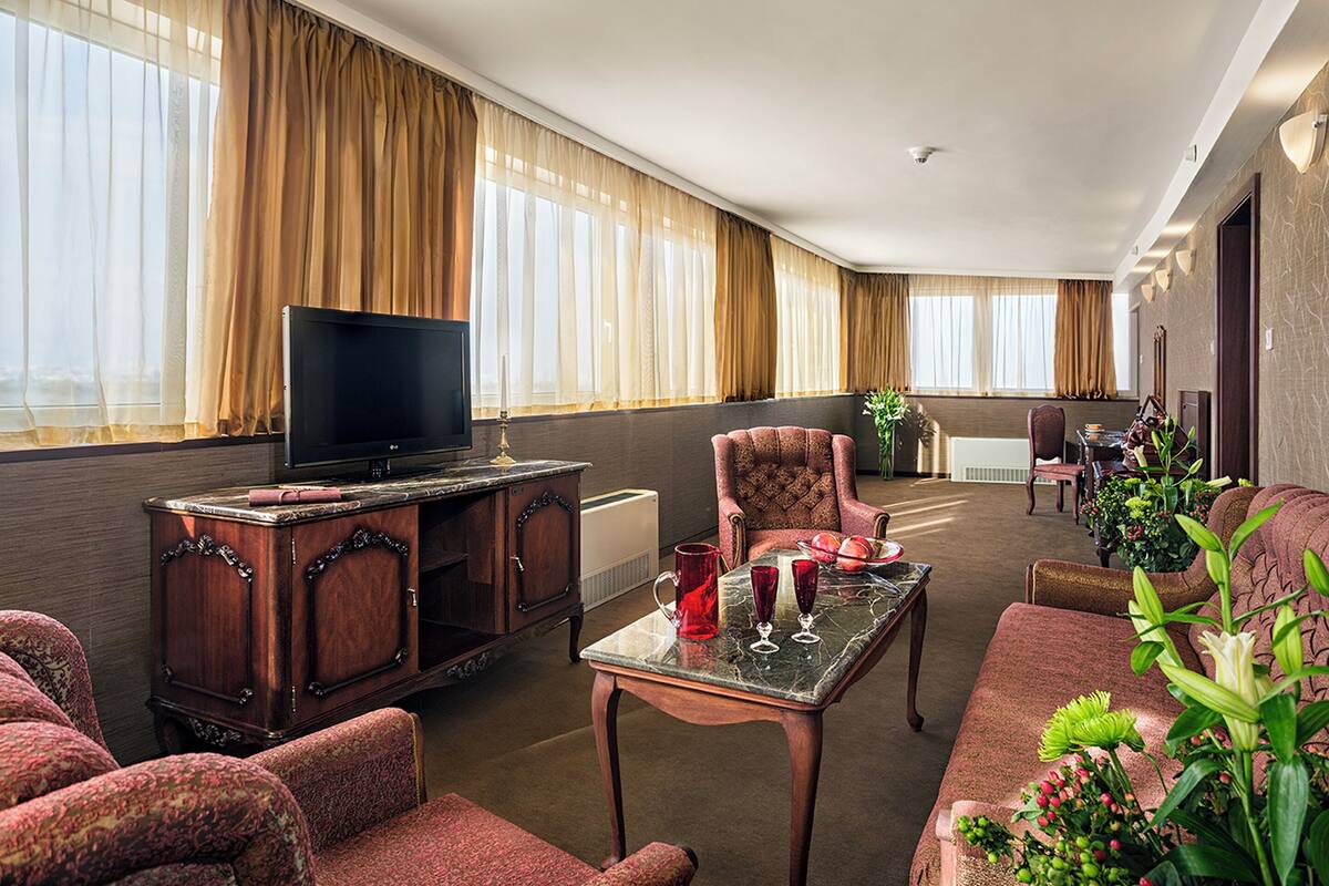 A hotel room with a flat-screen TV, a wooden cabinet, a sofa, a coffee table, and a dining area with chairs and a table.
