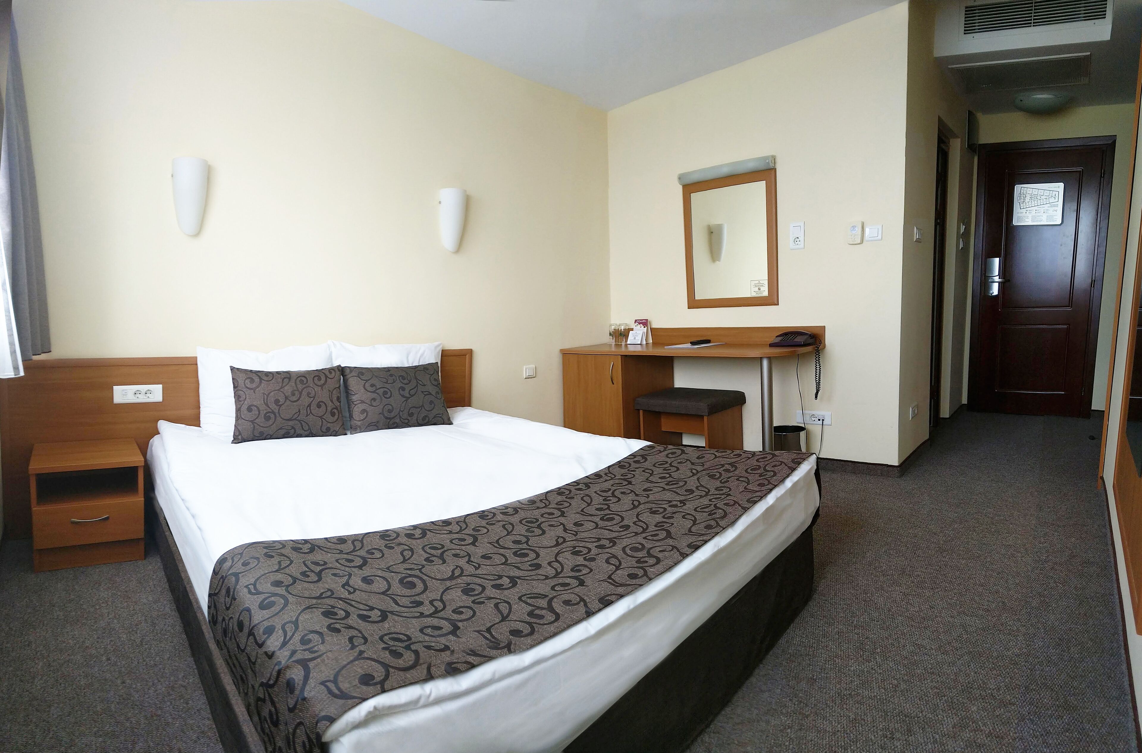Habitación de hotel con cama, mesita de noche, cómoda, espejo y puerta que da a otra habitación.