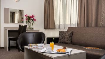 Habitación de hotel con una mesa de comedor dispuesta para el desayuno, un sofá, una silla, un escritorio y un espejo.