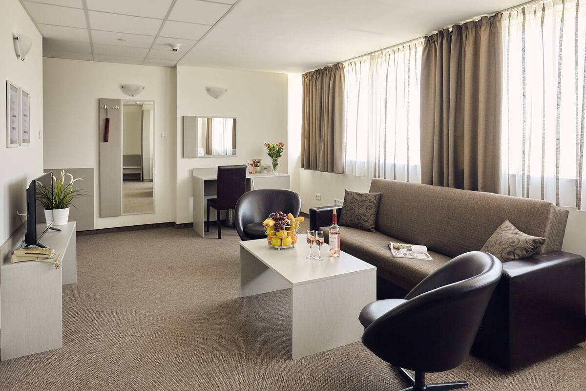 A modern hotel room with a sofa, a coffee table, a TV, and a desk with a chair.