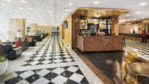 A hotel lobby with a checkered floor, a reception desk, seating areas, and a bar.