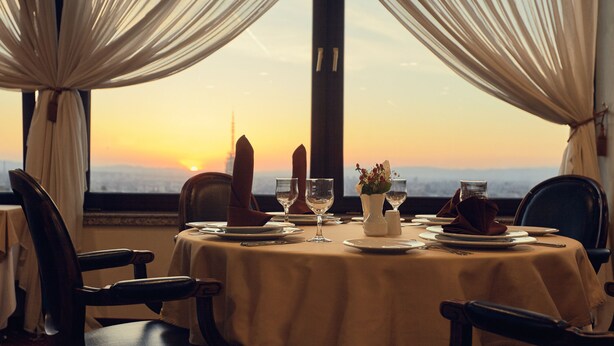 A table set for dinner with a sunset view through curtains.