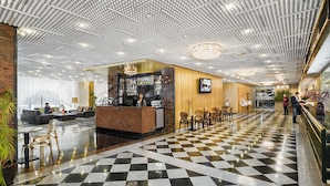 A hotel lobby with a checkered floor, a reception desk, seating area, and a bar.