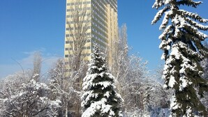 A tall building with a modern design, surrounded by snow-covered trees and a clear blue sky.