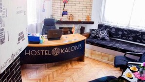 A hostel interior with a reception desk labeled 'HOSTEL KALONIS', a sofa, a chair, and a small table with a drink and a flower vase. - Apart Hotel Kalonis Skopje (Skopje)