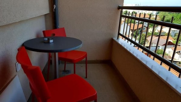 Un pequeño balcón con una mesa redonda y dos sillas rojas.