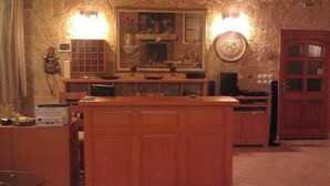 A kitchen with wooden cabinets, a central island, a built-in oven, and a wall-mounted clock. - Hotel Portal (Skopje)