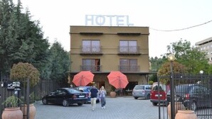A hotel entrance with a sign, a paved driveway, and parked cars. - Hotel Portal (Skopje)