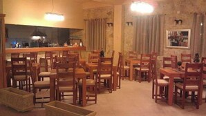 A dining area with wooden tables and chairs, a bar counter, and a stone wall. - Hotel Portal (Skopje)